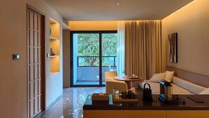 A modern hotel room with a glass door leading to a balcony, a sofa, a small table, and a coffee table with amenities. - Jiangnan House Chaozhou (Chaozhou)