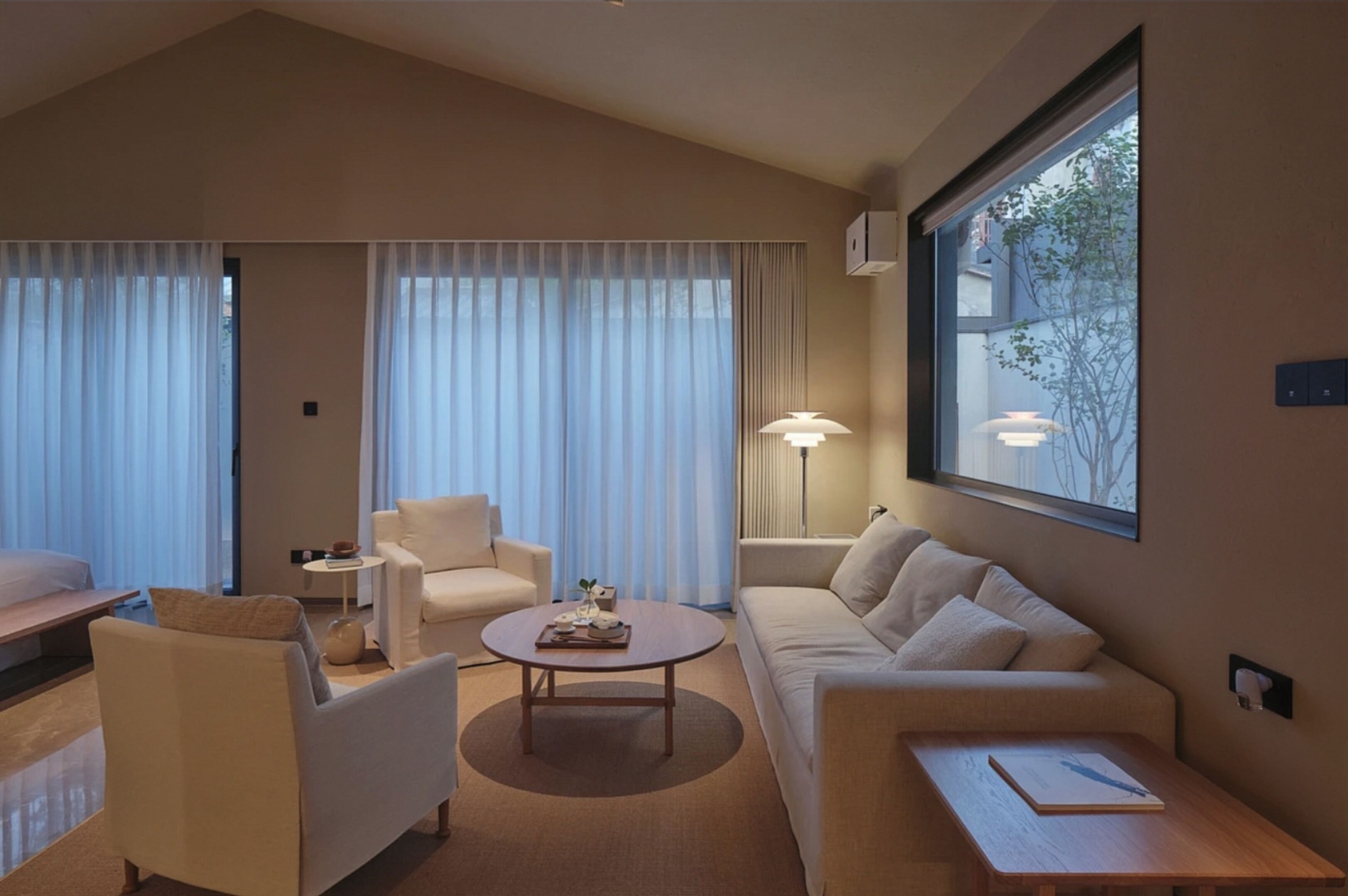 Una habitación de hotel moderna con sofá, sillones, una mesita de centro y una lámpara.