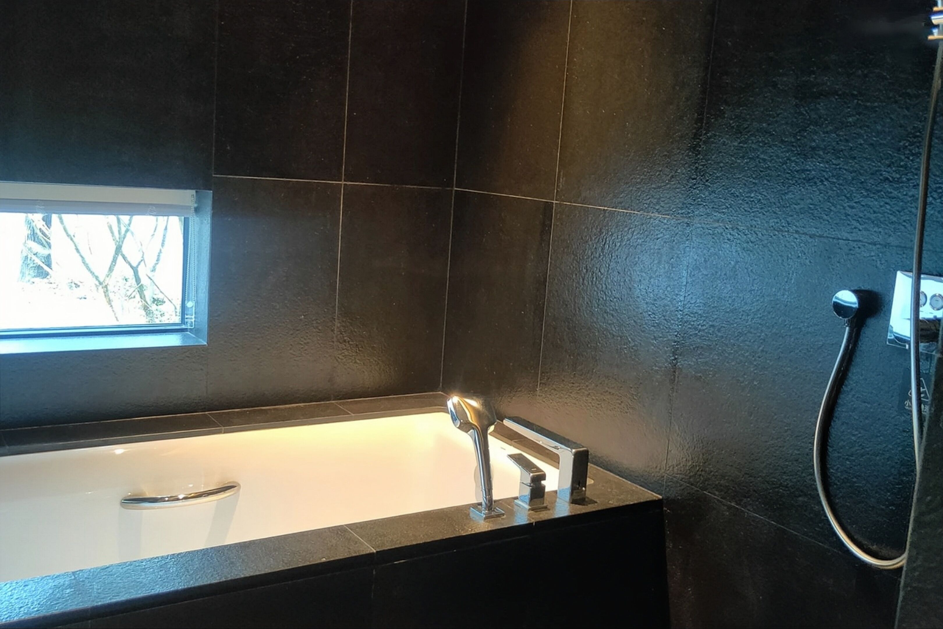 A modern bathroom with a bathtub, a handheld showerhead, and a window providing natural light.
