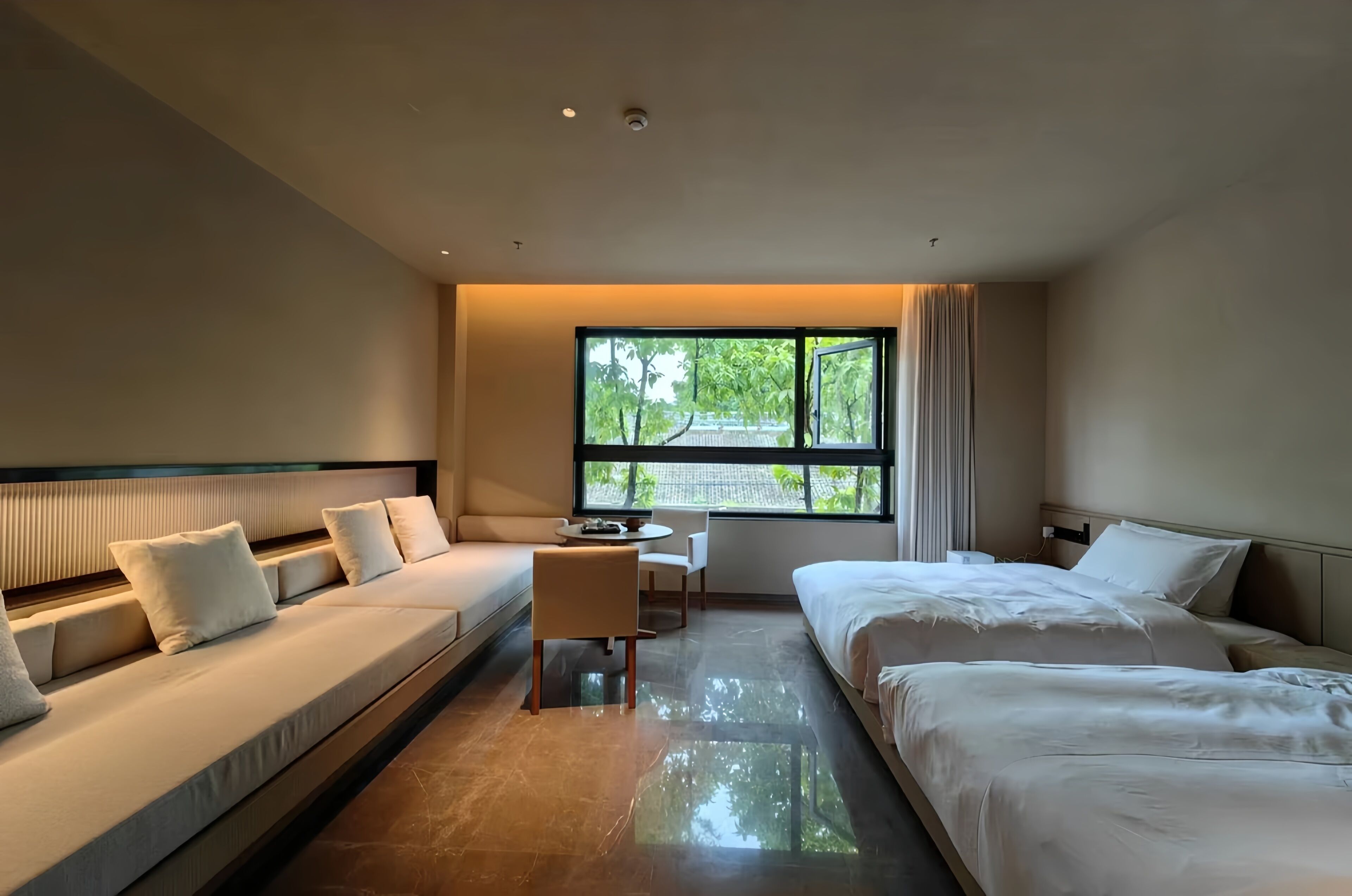 Una habitación de hotel moderna con sofá, cama, escritorio y un amplio ventanal con vistas a zonas verdes.