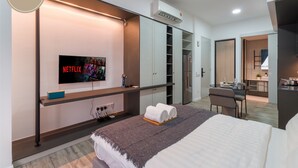 Een moderne hotelkamer met een bed, een aan de muur bevestigde televisie, een bureau met stoel en een kitchenette.
