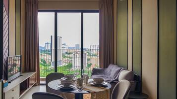A dining area with a table set for two, a television on a stand, and a city view through large windows.