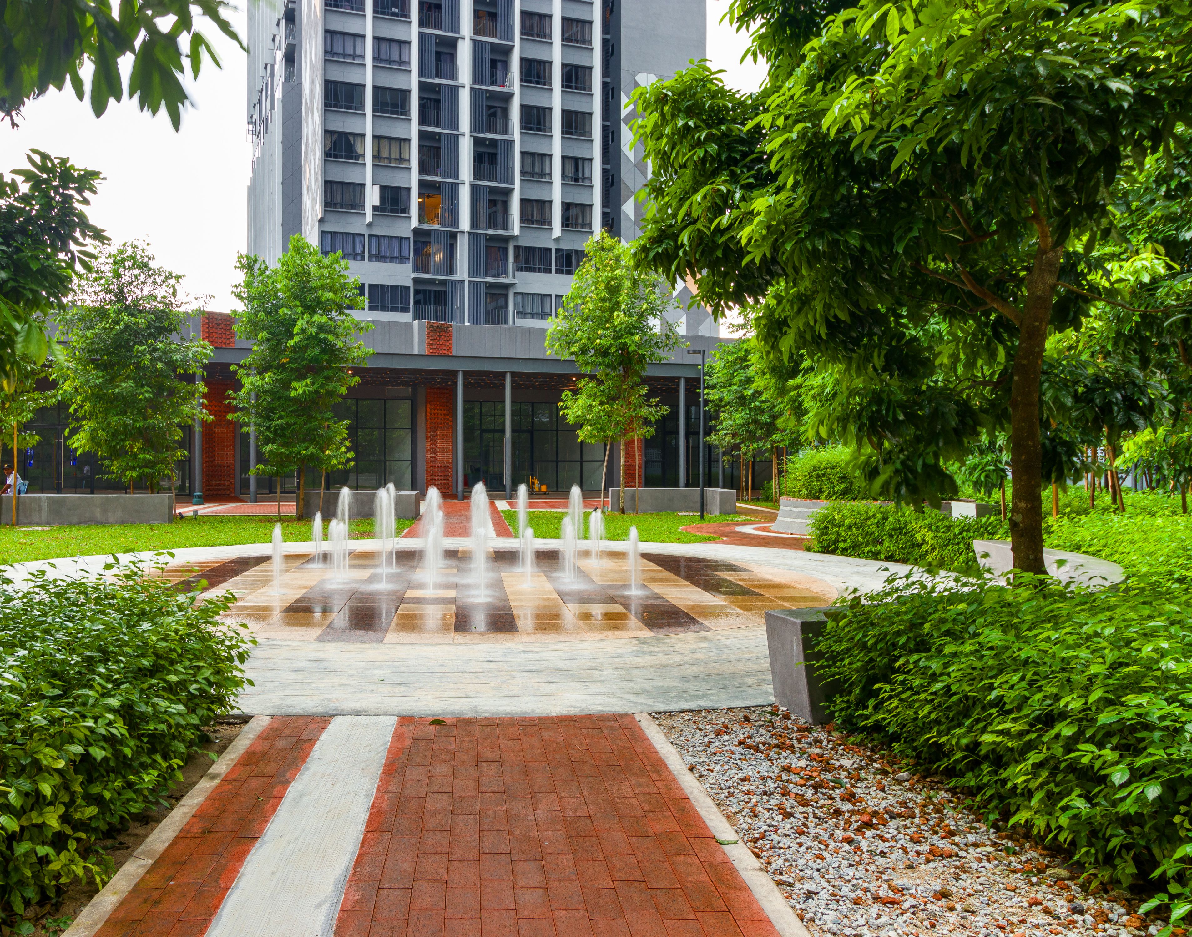 A modern building with a central water feature, surrounded by greenery and a paved walkway.