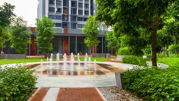 A modern building with a central water feature, surrounded by greenery and a paved walkway.