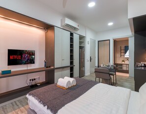 Een moderne hotelkamer met een bed, een aan de muur bevestigde televisie, een bureau met stoel en een kitchenette.