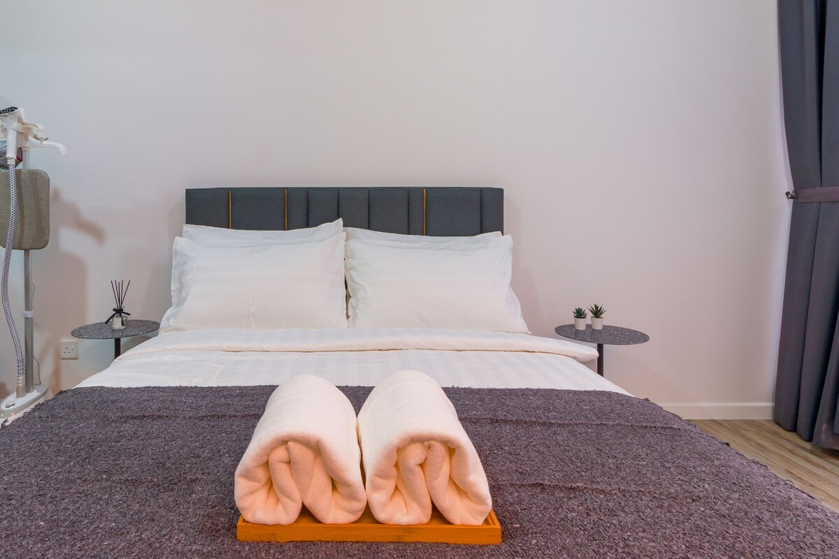 Een keurig opgemaakt bed met een paar gevouwen handdoeken op een dienblad, een nachtkastje met een lamp en een bijzettafeltje met twee planten in potten.