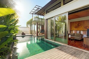 A modern pool area with glass walls, a wooden deck, and a cozy seating area with a sofa and a TV. - Eaze Villas (Pecatu)