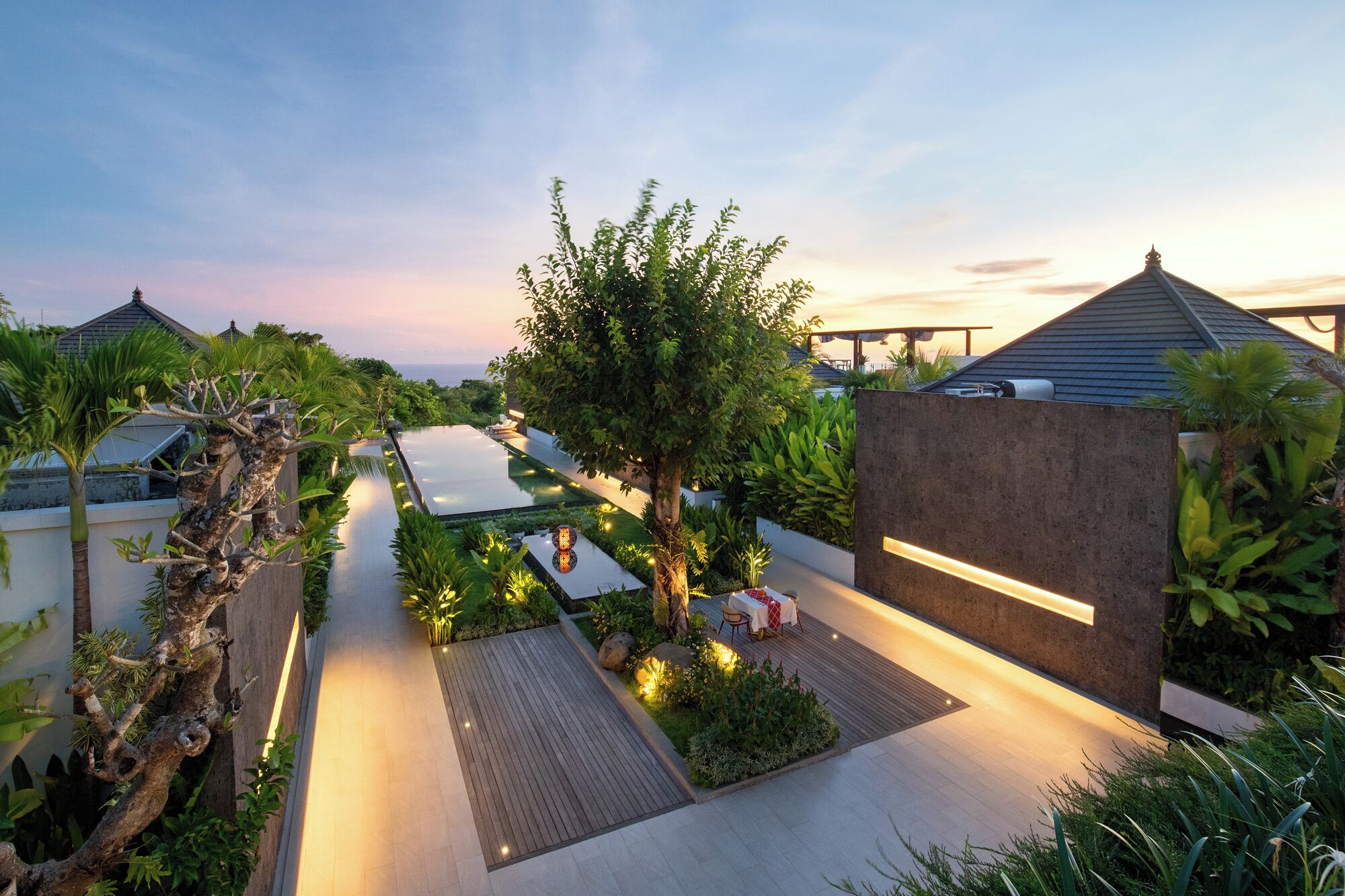 A modern resort with a swimming pool, lush greenery, and a well-lit pathway.