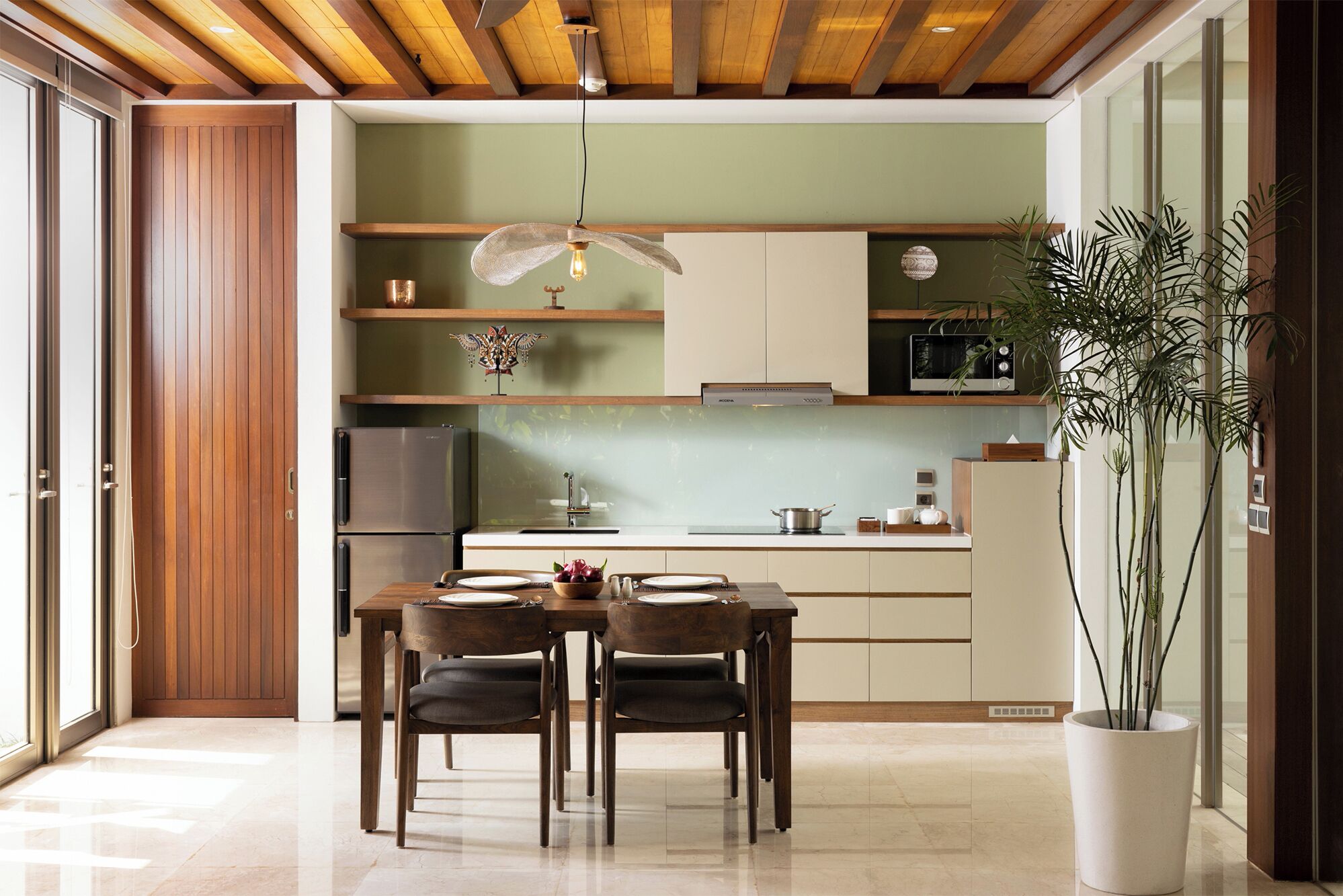 A modern kitchen with wooden cabinets, a dining table with chairs, a hanging light fixture, and a potted plant.