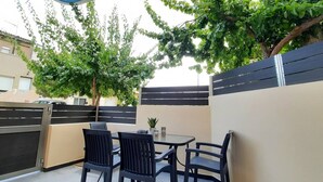 Un área de patio al aire libre con una mesa y sillas, rodeada por un muro bajo y árboles.