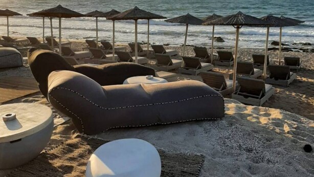 Un área de descanso junto a la playa con sillones y sombrillas, un espacio de estar circular y vistas al océano.