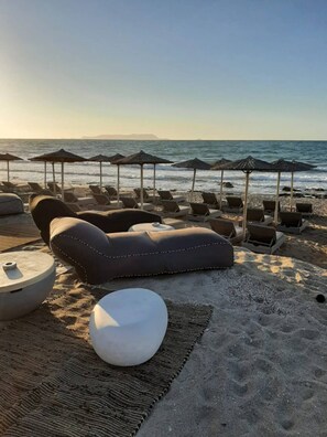A beachside lounge area with lounge chairs and umbrellas, a round seating area, and a view of the ocean.