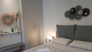 Un dormitorio con una cama, almohadas, una mesita de noche, una lámpara, un banco, un armario y adornos en la pared.