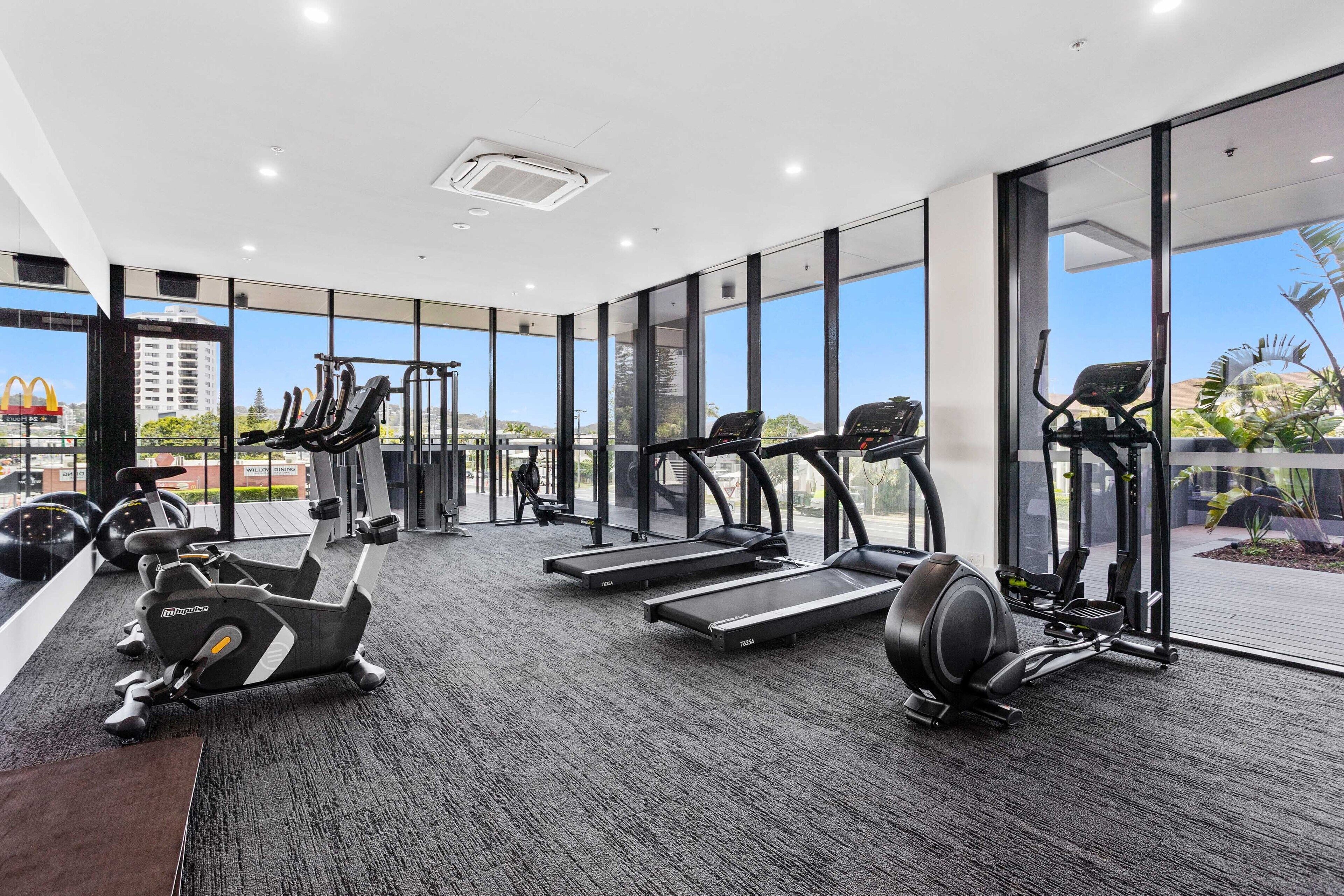 Une salle de sport moderne dotée de divers appareils d’exercice, de grandes fenêtres et offrant une vue sur le paysage urbain.