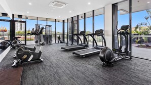 A modern gym with various exercise equipment, large windows, and a view of the cityscape. - 2 Bedroom Luxury in Burleigh Heads! (Gold Coast)