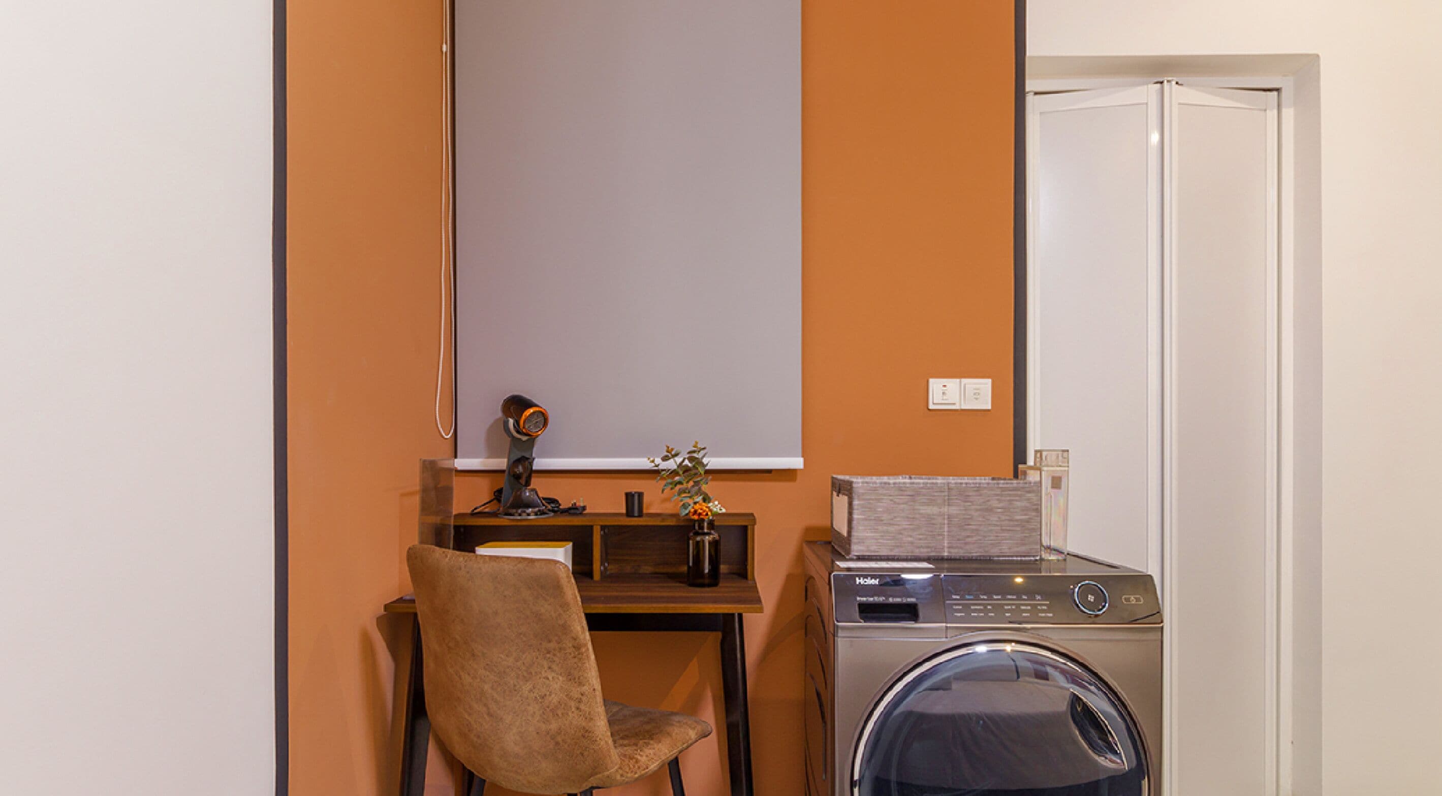 Una habitación compacta con lavadora, un escritorio pequeño con silla y una pizarra en la pared.