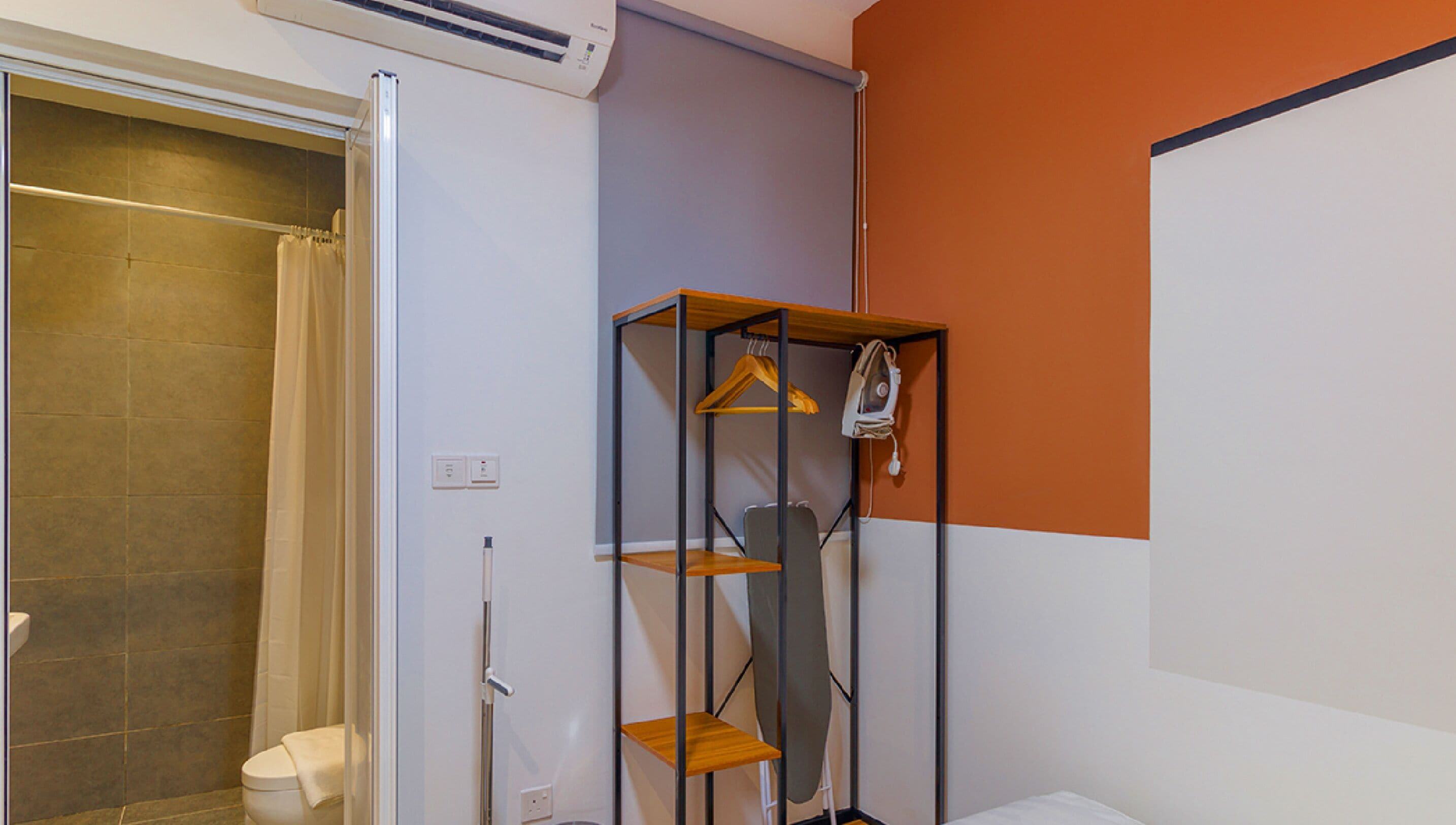 Une salle de bain équipée d’une douche, de toilettes et d’une étagère en bois où sont suspendus des vêtements.