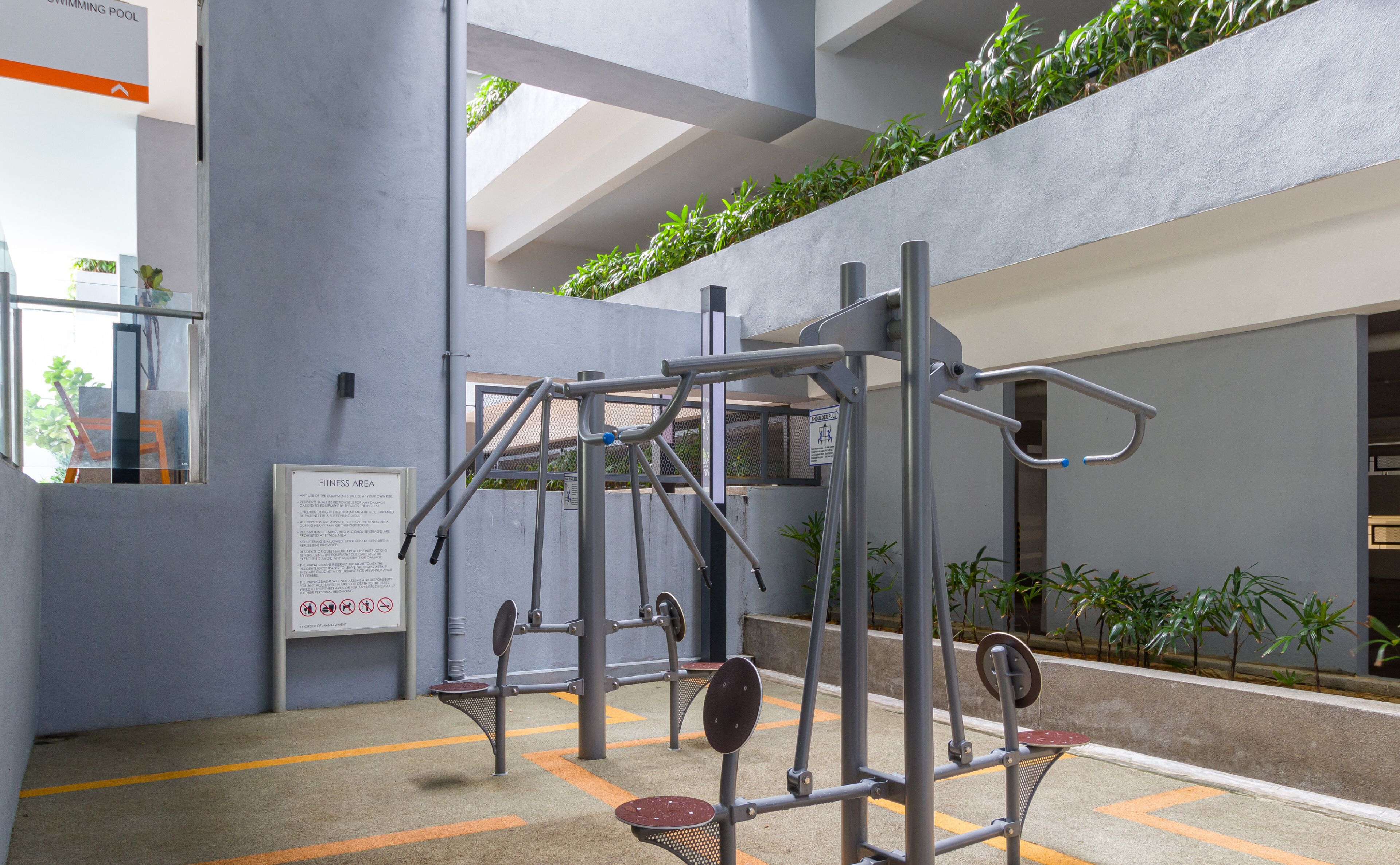 Un espace dédié à la remise en forme, équipé de matériel d’exercice, avec un panneau indiquant qu’il s’agit d’un espace de remise en forme, et une piscine visible au loin.