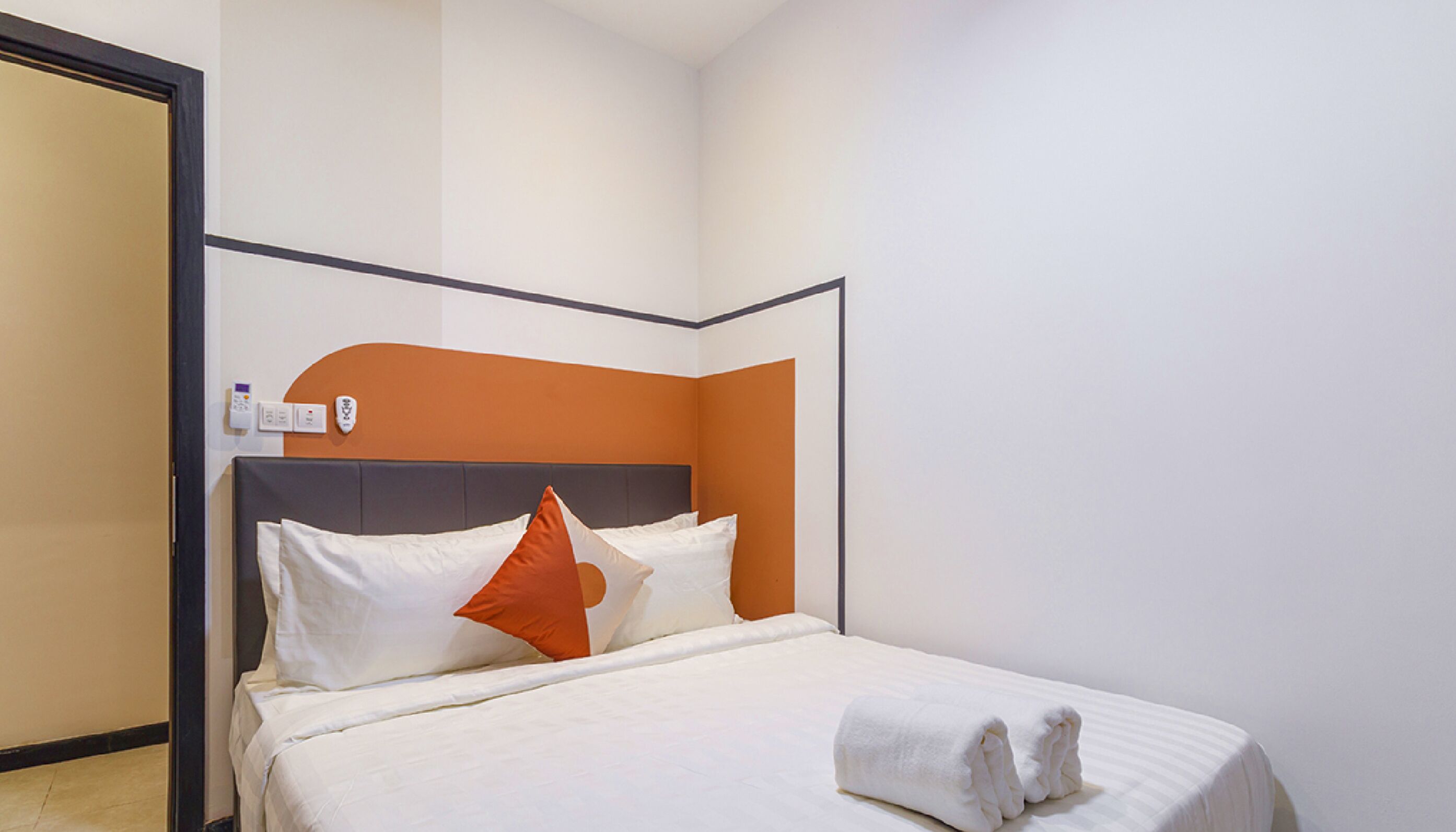 A hotel room with a bed, white bedding, an orange accent wall, and a black headboard.
