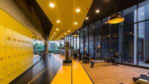 Un gimnasio con taquillas amarillas, equipo de ejercicio y ventanas amplias.