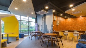 Un café moderno con un mural de ladrillo, asientos amarillos y luz natural que entra por amplias ventanas.