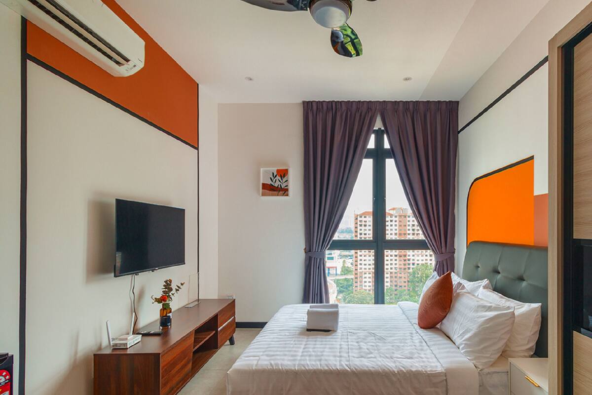 Une chambre d’hôtel moderne équipée d’un lit, d’une télévision, d’un bureau avec un ordinateur portable et d’une fenêtre avec des rideaux.