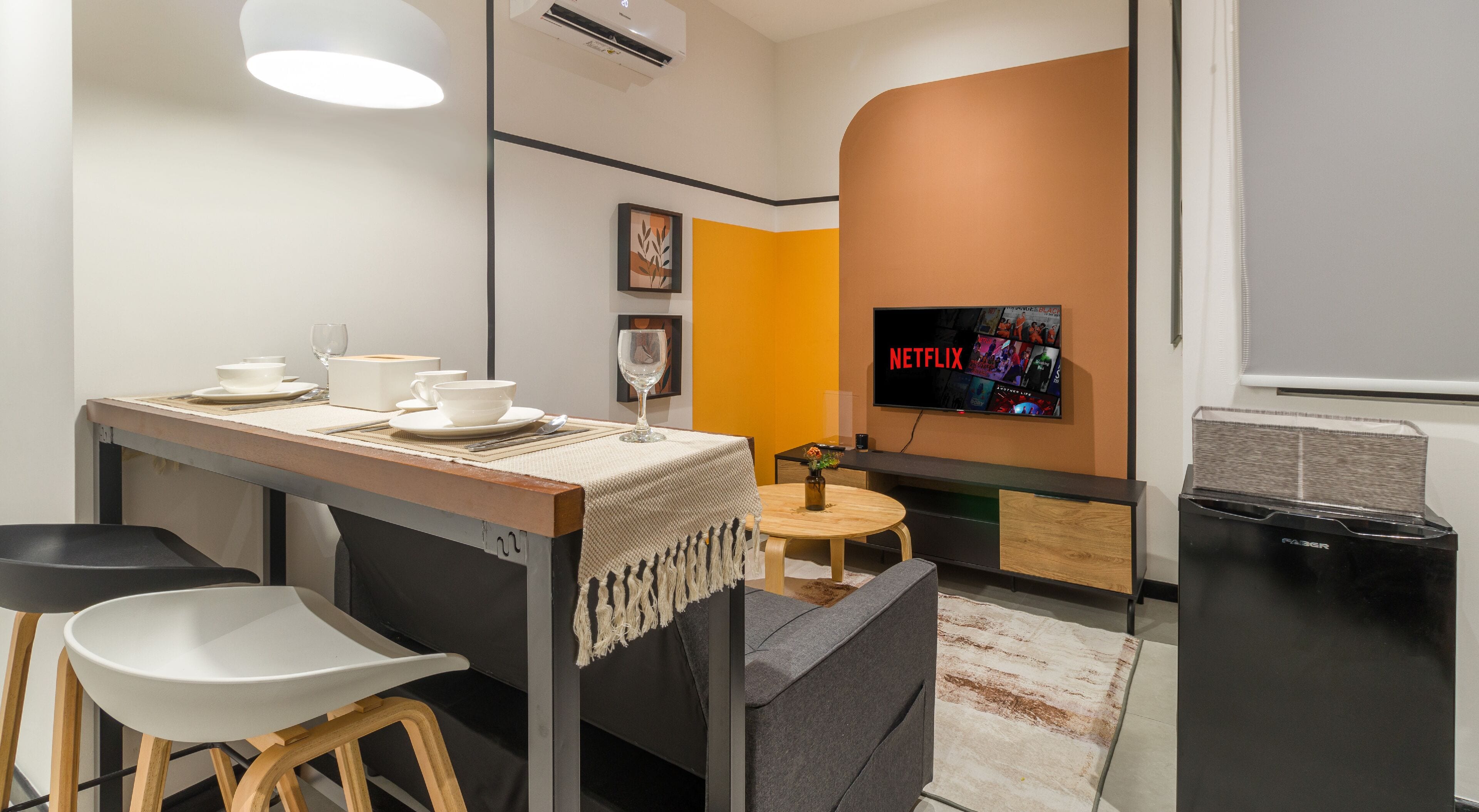 A modern hotel room with a dining area, a TV displaying Netflix, and a trash bin.