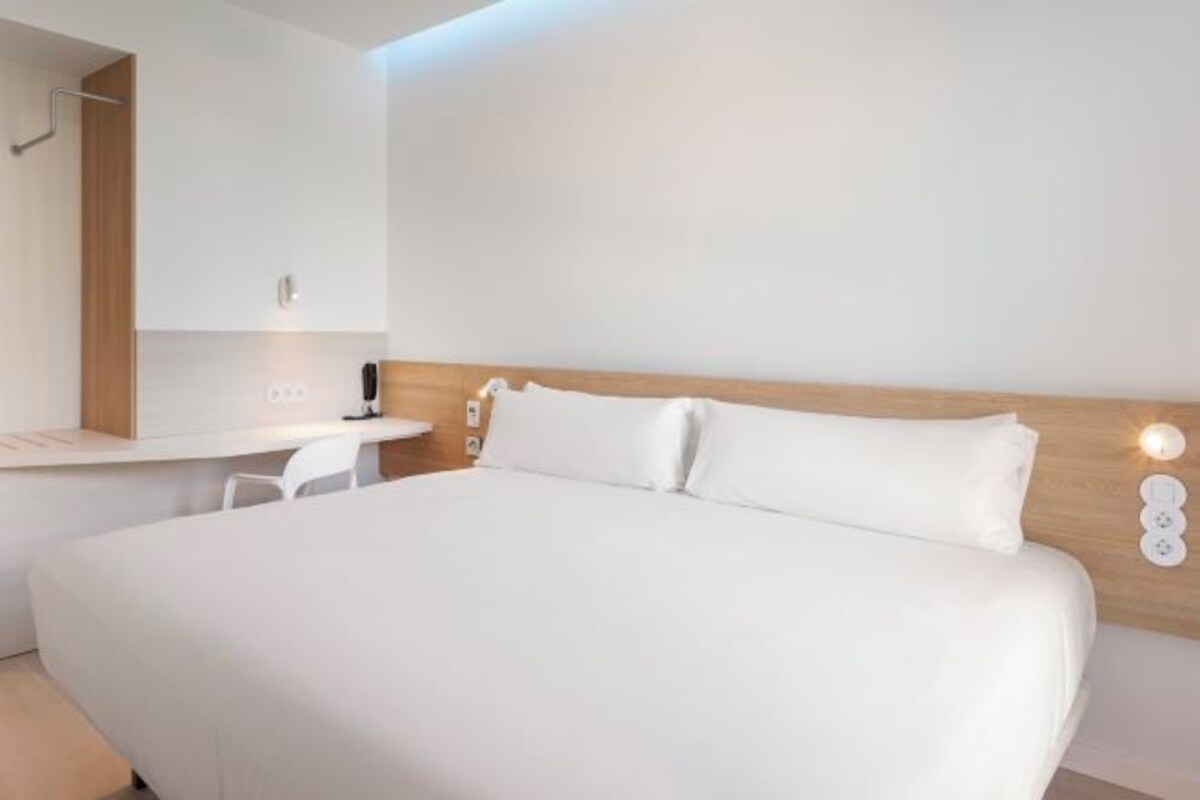 A modern hotel room with a large bed, a desk, and a mirror.