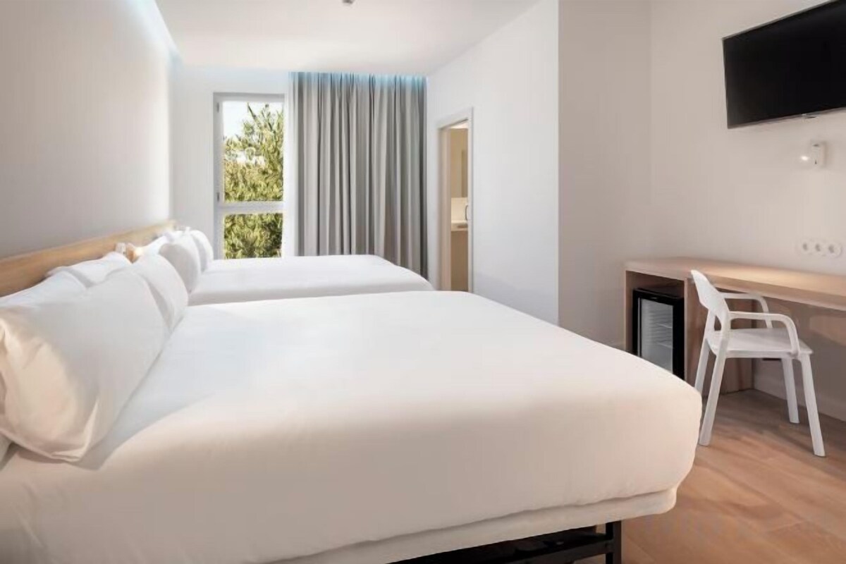 Habitación de hotel con dos camas, un escritorio, una silla y un televisor montado en la pared.