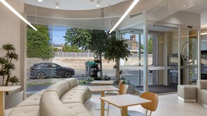 A modern interior with a sofa, tables, and chairs, large windows with a view of the street and trees. - B&B Hotel Lleida (Lleida)