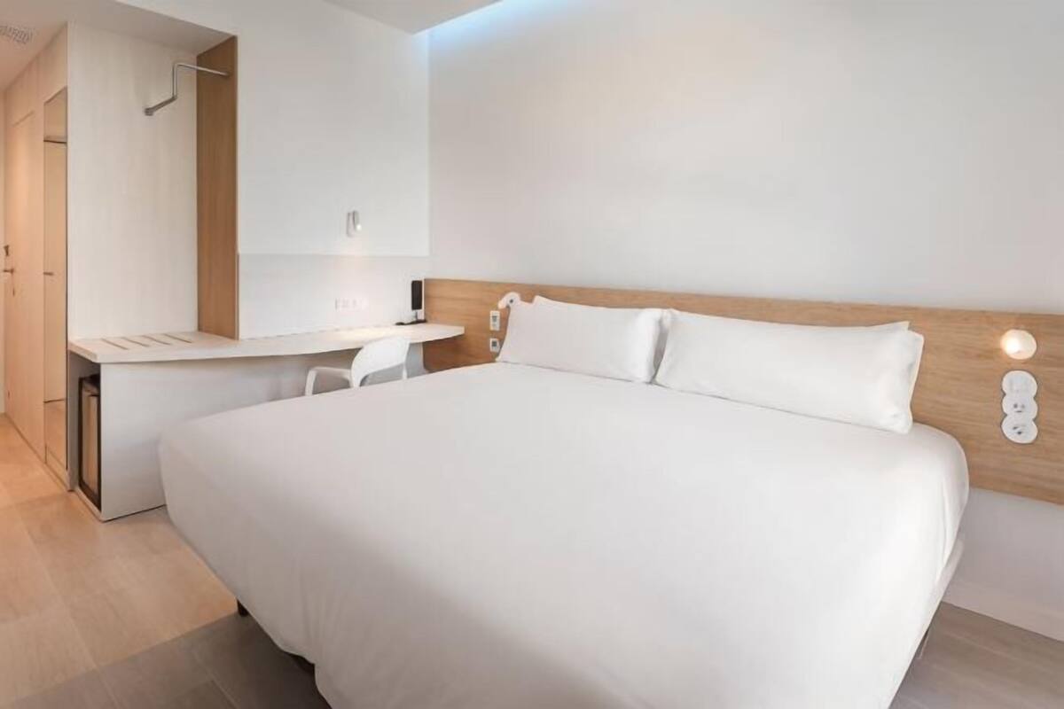 A modern hotel room with a large bed, a desk, and a mirror.