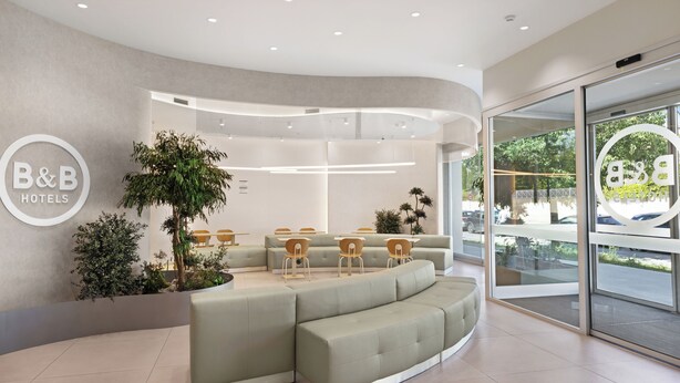 A modern hotel lobby with a curved seating area, a reception desk, and a large window offering a view of the outdoors. - B&B Hotel Lleida (Lleida)