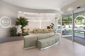 A modern hotel lobby with a curved seating area, a reception desk, and a large window offering a view of the outdoors. - B&B Hotel Lleida  (Lleida)