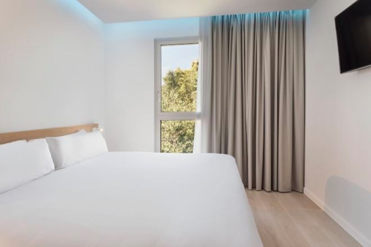 A hotel room with a large bed, a window with curtains, and a flat-screen TV mounted on the wall.