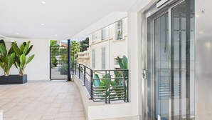 Zona interior àmplia amb terra de rajola, un ascensor de vidre i una barana metàl·lica amb vista a un jardí.