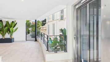 A spacious indoor area with a tiled floor, a glass elevator, and a metal railing overlooking a garden.