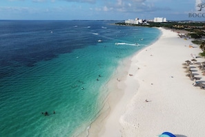 Une plage aux eaux turquoise et limpides, un rivage sablonneux et une vue lointaine sur la ville.
