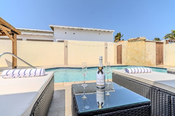 A rooftop pool area with lounge chairs, a bottle of wine, and glasses.