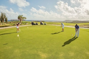 Un terrain de golf avec des joueurs, un ciel dégagé et des montagnes à l’horizon.