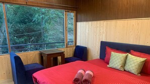 Camera da letto con un letto grande, due sedie, un tavolino e una finestra vista foresta.