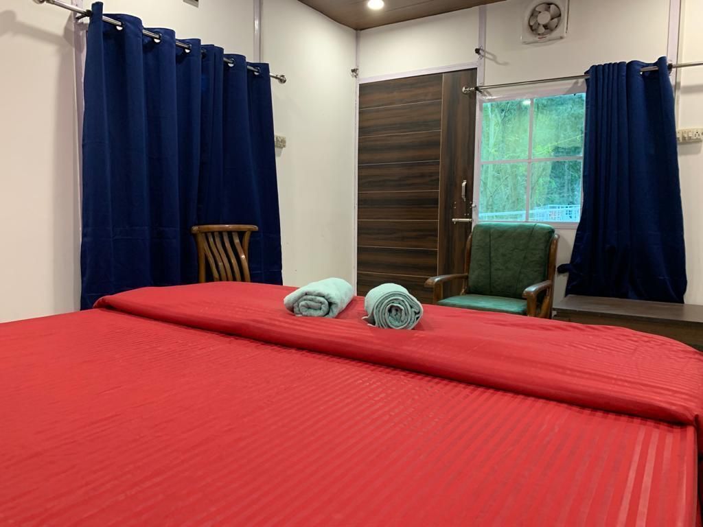 A room with a bed, two chairs, a window with curtains, and a door.