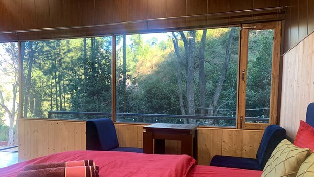 Una stanza con un letto grande, un tavolino e vista su una foresta attraverso ampie finestre.