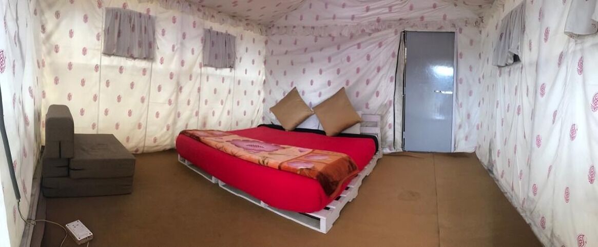 A small, single-bed room with a red bedspread, two pillows, and a grey sofa.