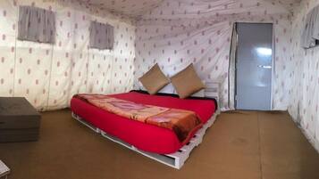 A small, single-bed room with a red bedspread, two pillows, and a grey sofa.