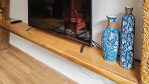Un téléviseur à écran plat posé sur une étagère en bois, deux vases bleus à motifs et un panier tressé.