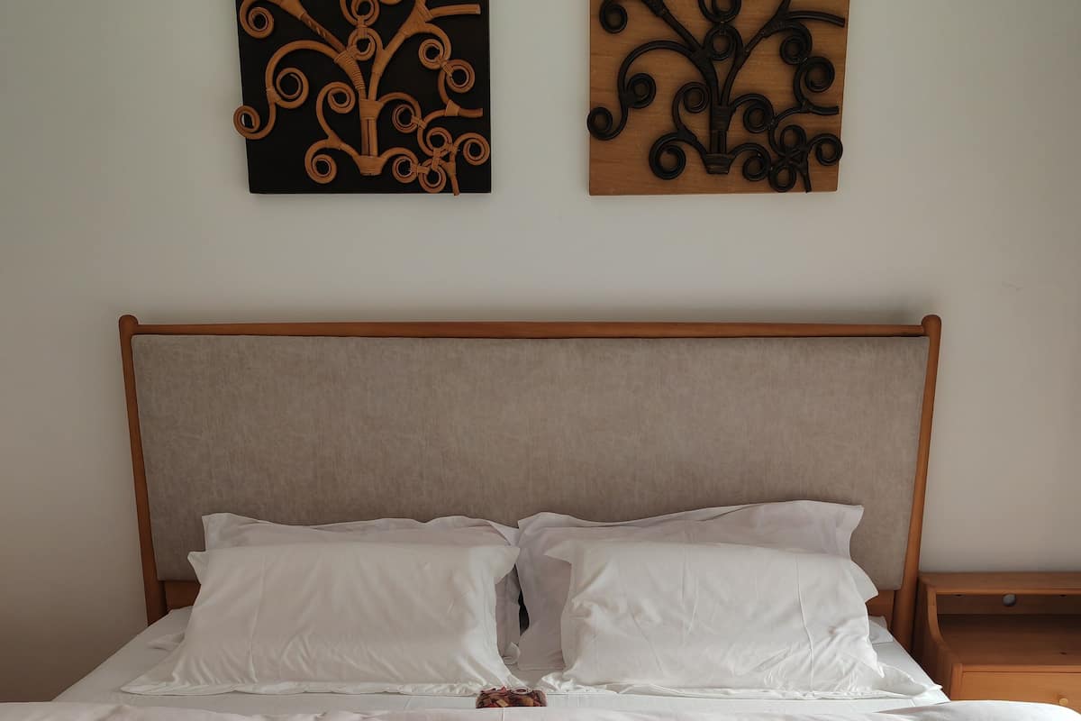 Una cama bien hecha con sábanas blancas, cabecero de madera y dos obras de arte en la pared.