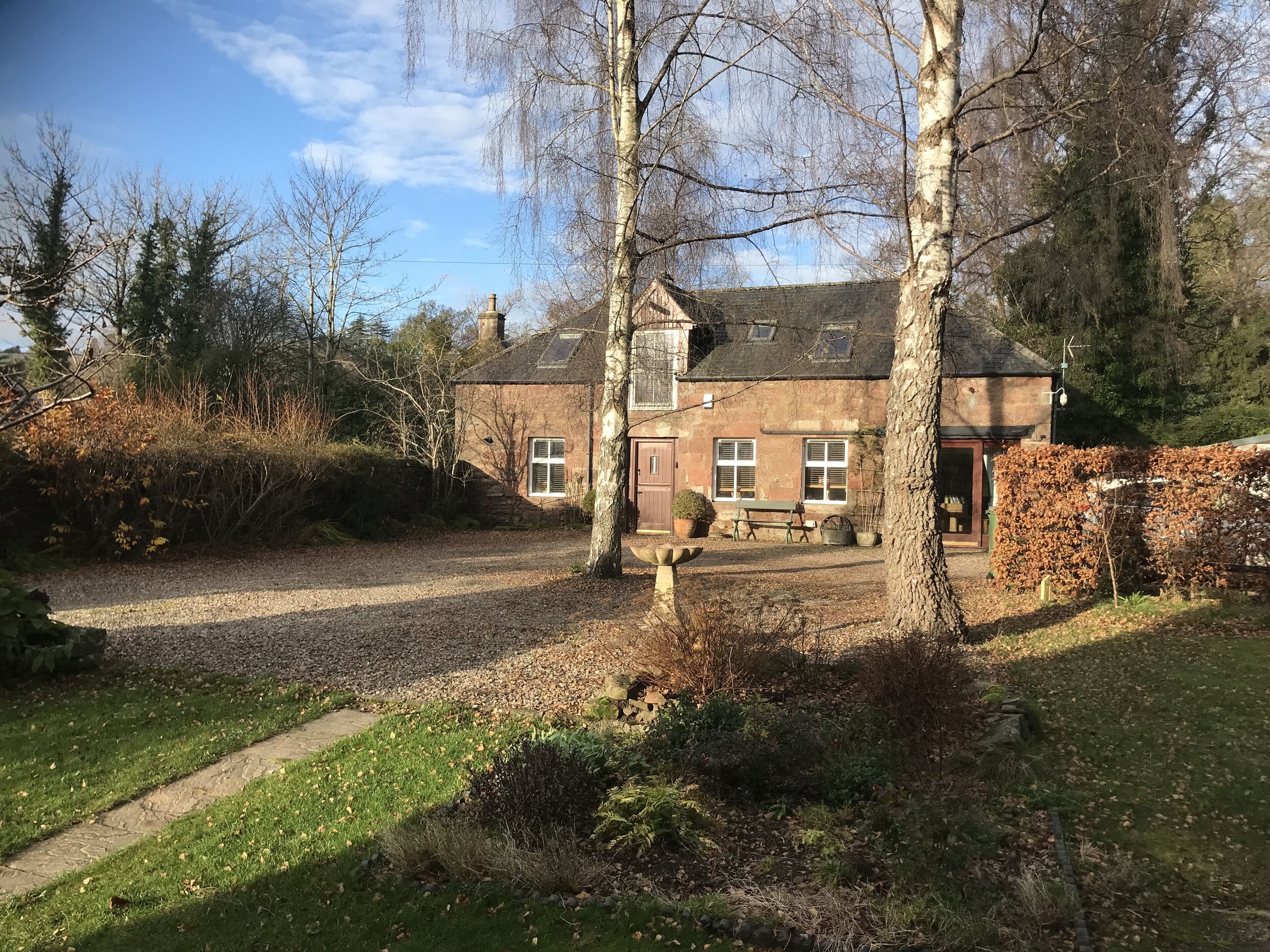 Een stenen huis met een grindpad, een bankje en een kleine tuin.