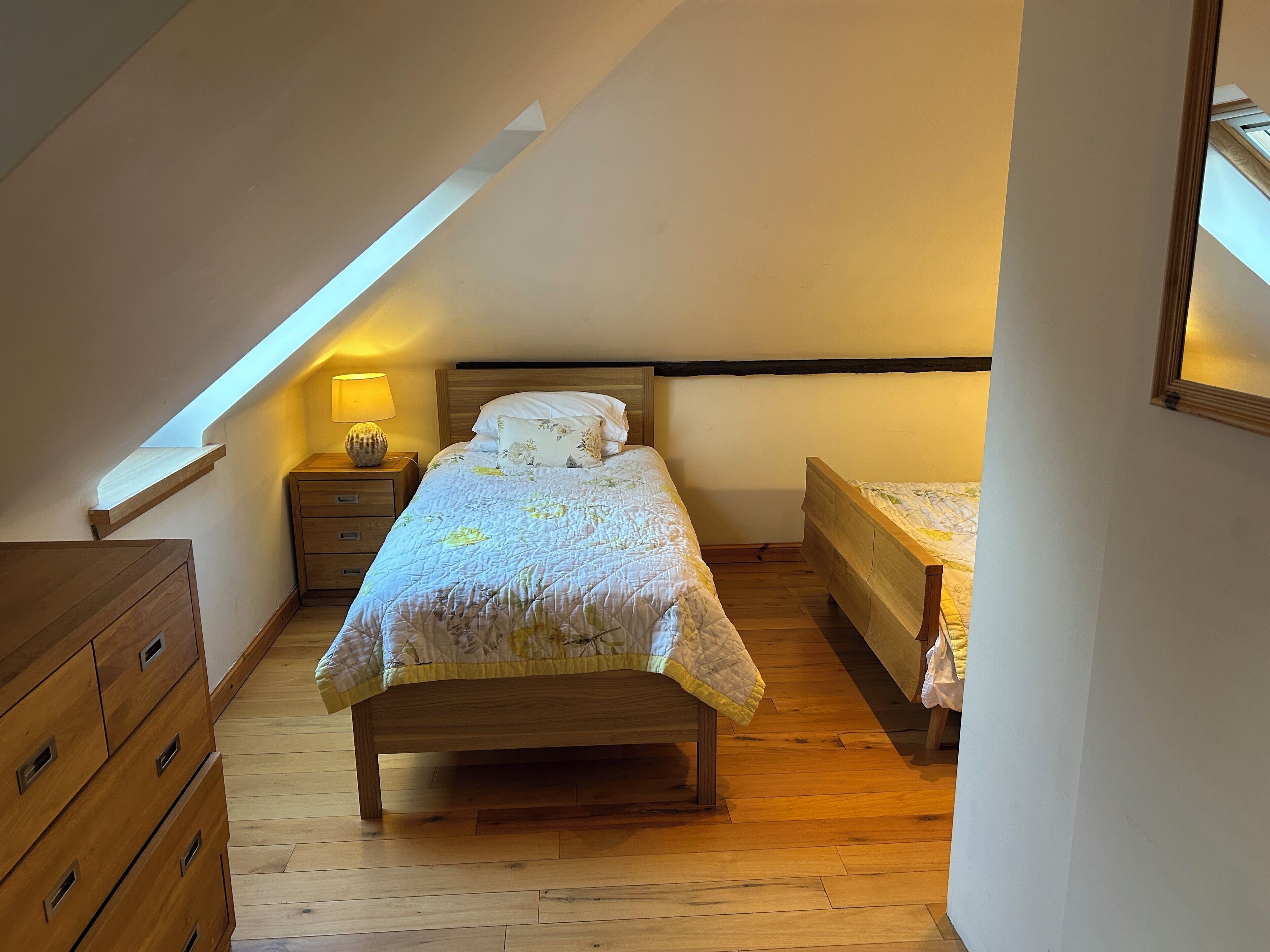 A bedroom with a sloped ceiling, a wooden bed, a nightstand with a lamp, and a dresser.