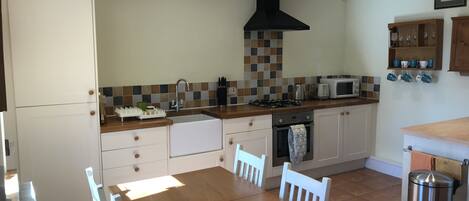 A modern kitchen with a wooden table, white chairs, a built-in oven, a microwave, and a gas stove.