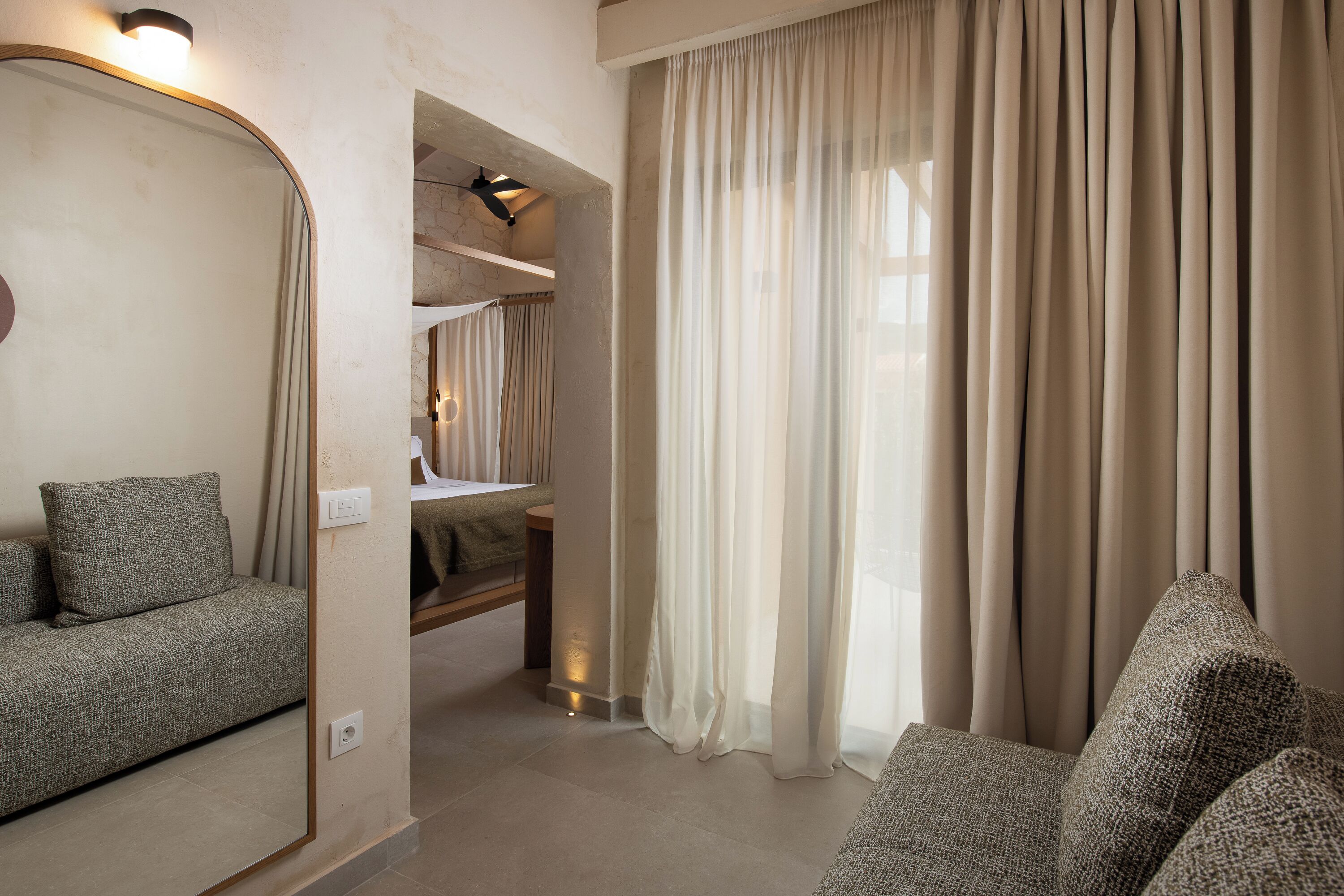 A hotel room with a sofa, a mirror, a bed, and a window with curtains.